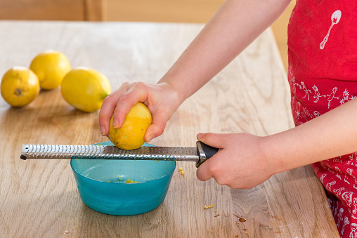 Little girl grating zest of organic lemon on kitchen table