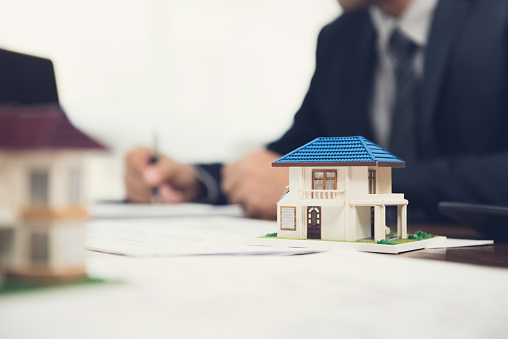 Real estate agent signing document with house model on the table
