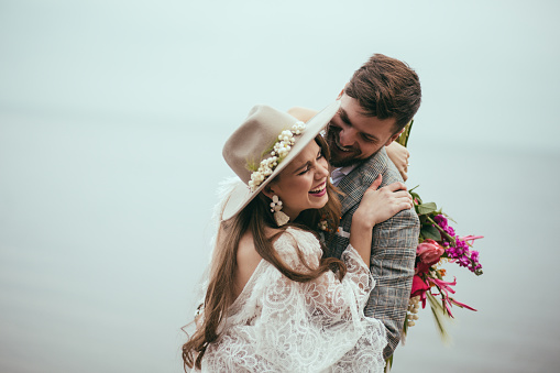 beautiful happy bride and groom in boho style laughing at lake