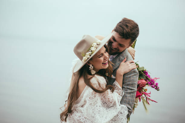 beautiful happy bride and groom in boho style laughing at lake - fotos de boho imagens e fotografias de stock