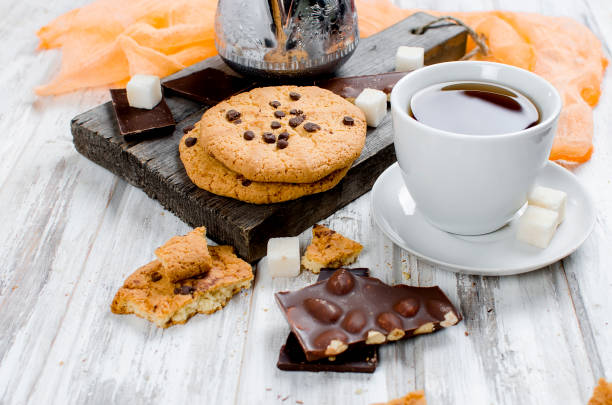 Cup of black tea, and biscuits with chocolate drops, chocolate on white wooden table. top view.  copy space