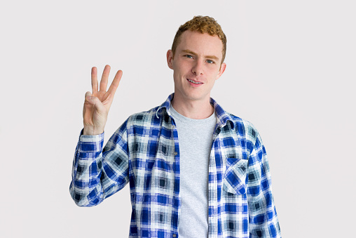 Smiling red haired Caucasian man showing three fingers. Young startuper counting three. Counting concept