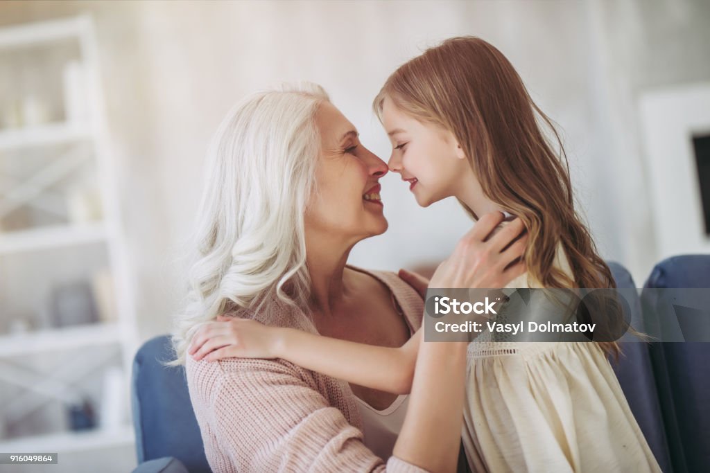 Little girl with grandmother Little cute girl and her grandmother are spending time together at home. Having fun, hugging and smiling while sitting on sofa. Grandmother Stock Photo