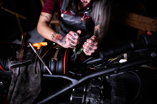 Tattoed female mechanic in auto repair shop is customizing motorcycle engine.