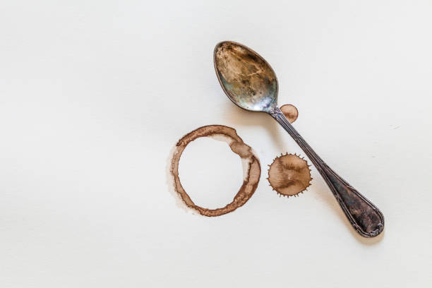 Old spoon, coffee drips and stains on textured white paper. There is a circle left by a dirty coffee cup and two dried coffee drops beside the spoon. Predominant colors are brown and white. Macro-photography DSRL studio photo taken with Canon EOS 5D Mk II and Canon EF 100mm f/2.8L Macro IS USM