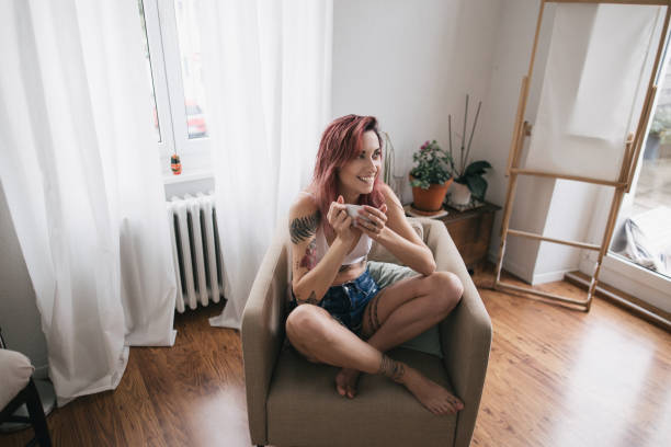 heureuse jeune femme tenant la tasse de café et de regarder loin dans appartement confortable - the human body photos photos et images de collection