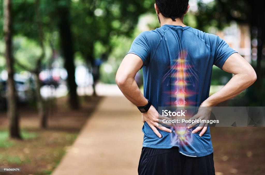 He's overdone it this time with his training Rear view shot of a sporty young man holding his back in pain while exercising outdoors Spine - Body Part Stock Photo