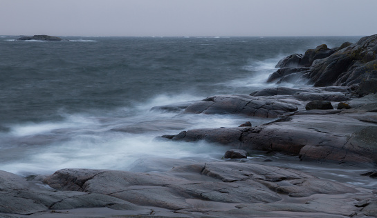 Waves of a stormy black autumn sea hit the shore line black rocks and turns into white water spray in the wind