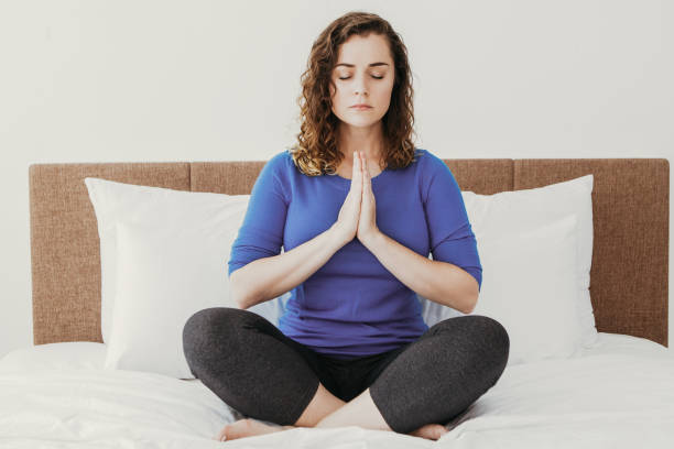 istock Beautiful Woman Meditating in Lotus Pose on Bed 916064582