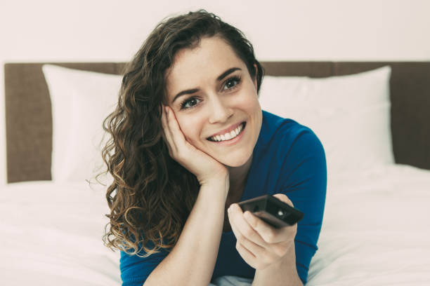 istock Smiling Beautiful Woman Watching TV on Bed 916064754
