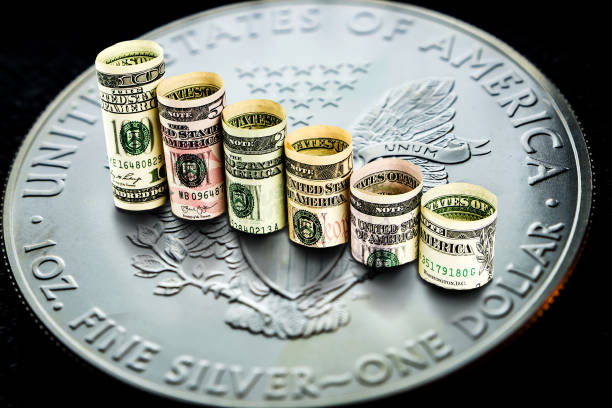 silver american eagle coin with rolls of dollar banknotes forming declinig steps closeup of silver american eagle coin with a chart reflection on its surface with green and red bars and rolls of dollar banknotes forming declinig steps dollar bill eagle stock pictures, royalty-free photos & images