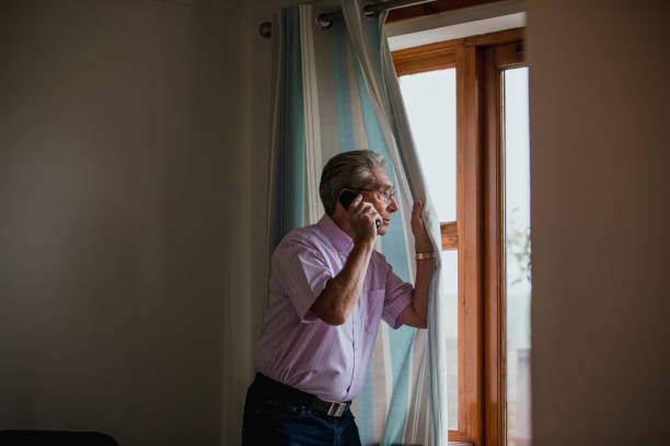 Senior Man on Telephone A senior man uses the telephone whilst peeking out of the window. neighborhood crime watch stock pictures, royalty-free photos & images