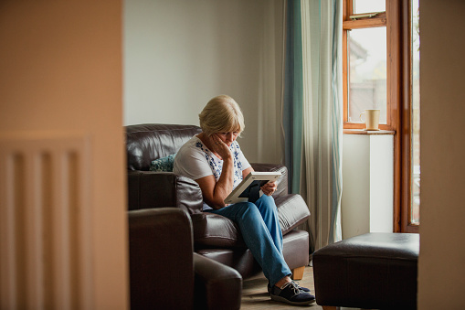 A senior woman sits in the living room and looks at a photo frame.