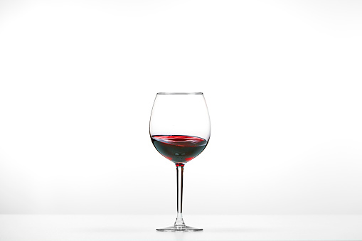 A glass on a thin leg with red wine on white background. 3D rendering