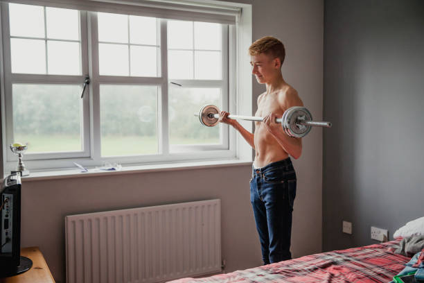 Teenage Boy Lifting Weights A teenage boy lifts weights in his bedroom. human muscle photos stock pictures, royalty-free photos & images