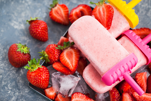 Delicious strawberry popsicles ice cream with ice and  fresh berries around, gray background