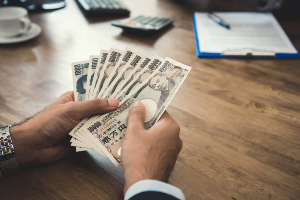 uomo d'affari mani che contano denaro, banconote in yen giapponesi, alla scrivania - simbolo dello yen foto e immagini stock