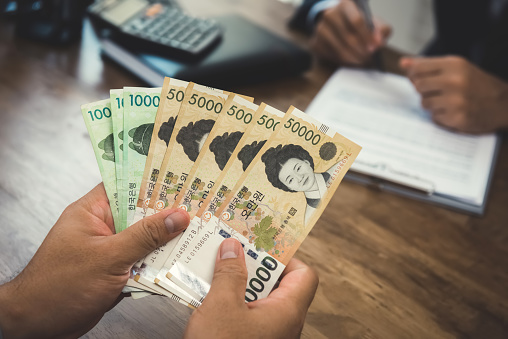 Hands of businessman holding money, South Korean Won currency, while making contract with his partner - financial, loan and bribery concept