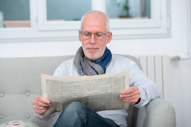 istock handsome mature man reading a newspaper on sofa 916081016
