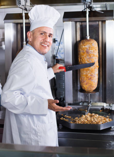 Cheerful mature man cook cutting kebab meat on kitchen in fast food cafe