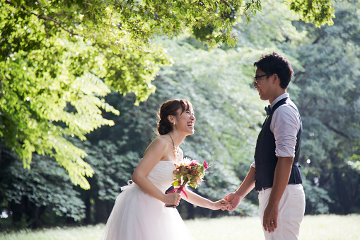 Japanese man is taking a hand of Japanese woman wearing wedding dress. She is holding a boupuet with the other hand.