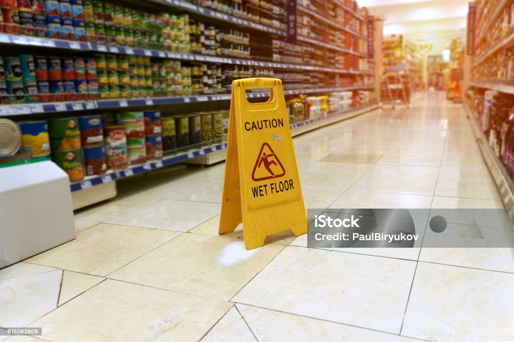 close up Yellow sign - caution. Wet floor is in the supermarket against the background of blurry products standing on the shelves Falling Stock Photo