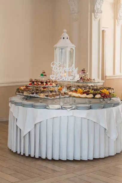 Candybar in a restaurant. Decorated white table fool of sweet pastry. Wedding sweets