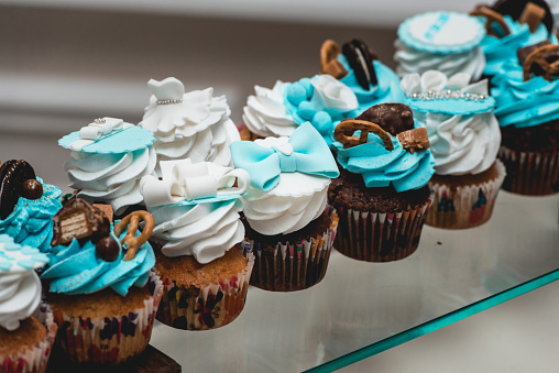 rows of birthday cupcake with butter white and blue cream icing on a glass stand. Wedding candy bar. Selective focus