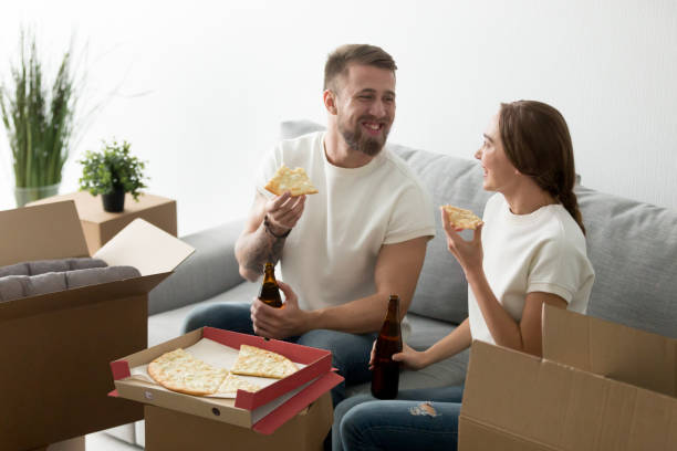 proprietari di case felici che mangiano pizza al formaggio bevendo birra che celebra h - two party system foto e immagini stock