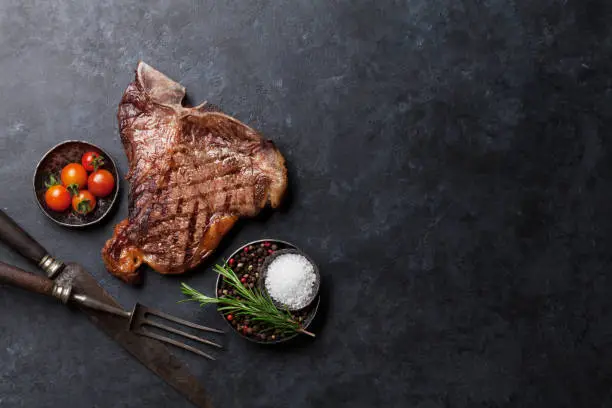 Grilled T-bone steak on stone table. Top view with copy space