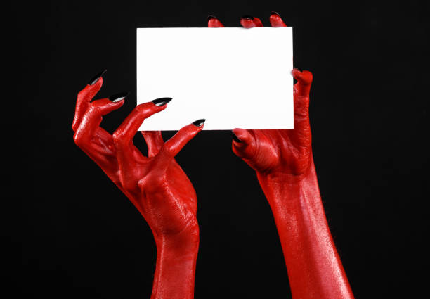 istock Halloween theme: Red devil hand with black nails holding a blank white card on a black background 916108182
