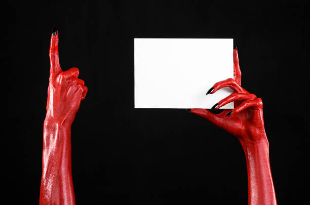 istock Halloween theme: Red devil hand with black nails holding a blank white card on a black background 916112234