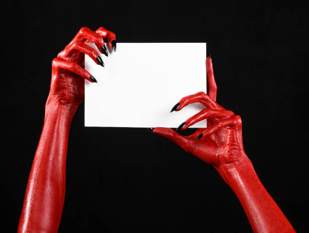 istock Halloween theme: Red devil hand with black nails holding a blank white card on a black background 916112932