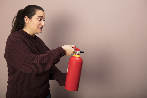 Woman with a shocked expression holding a fire extinguisher pointed towards blank copy space in a profile view
