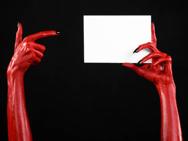 istock Halloween theme: Red devil hand with black nails holding a blank white card on a black background 916113540