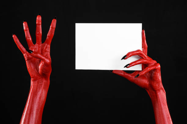 istock Halloween theme: Red devil hand with black nails holding a blank white card on a black background 916115332