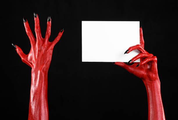 istock Halloween theme: Red devil hand with black nails holding a blank white card on a black background 916115820