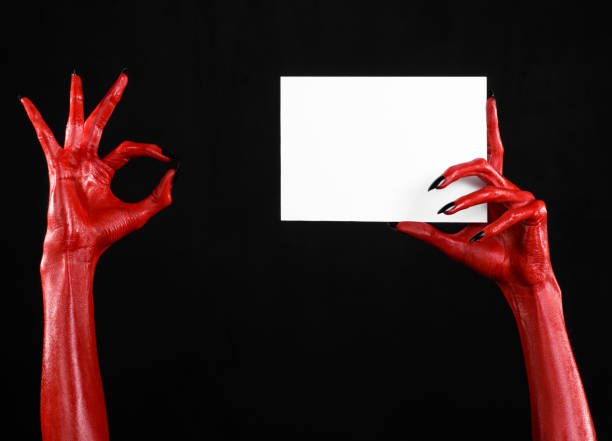 istock Halloween theme: Red devil hand with black nails holding a blank white card on a black background 916116458