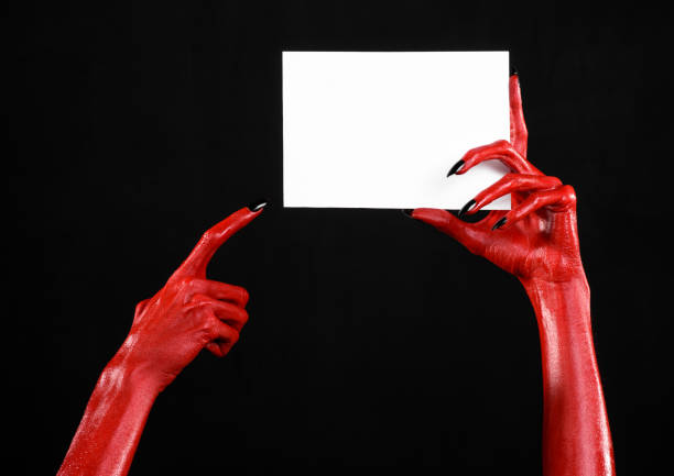 istock Halloween theme: Red devil hand with black nails holding a blank white card on a black background 916116908