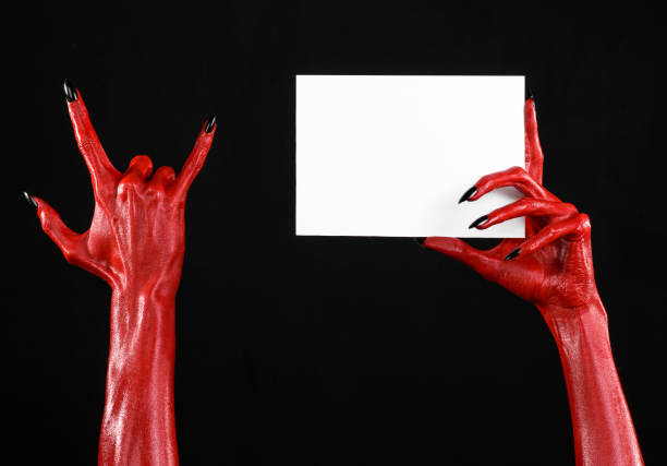 istock Halloween theme: Red devil hand with black nails holding a blank white card on a black background 916117094