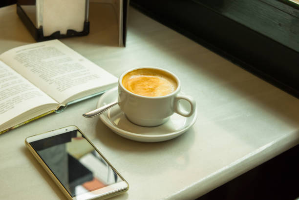 istock White Cup with Cappuccino on Table with Open Book Smartphone on 916118062