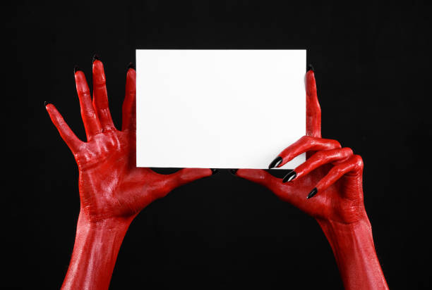 istock Halloween theme: Red devil hand with black nails holding a blank white card on a black background 916125128