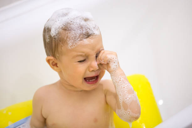 Cute toddler in tears crying taking a bath in bathtub Cute toddler in tears crying taking a bath in bathtub, scared kid afraid of water in bathroom touching irritated by shampoo foam eyes, sad emotional baby screaming weeping in tantrum while bathing wiping tears stock pictures, royalty-free photos & images