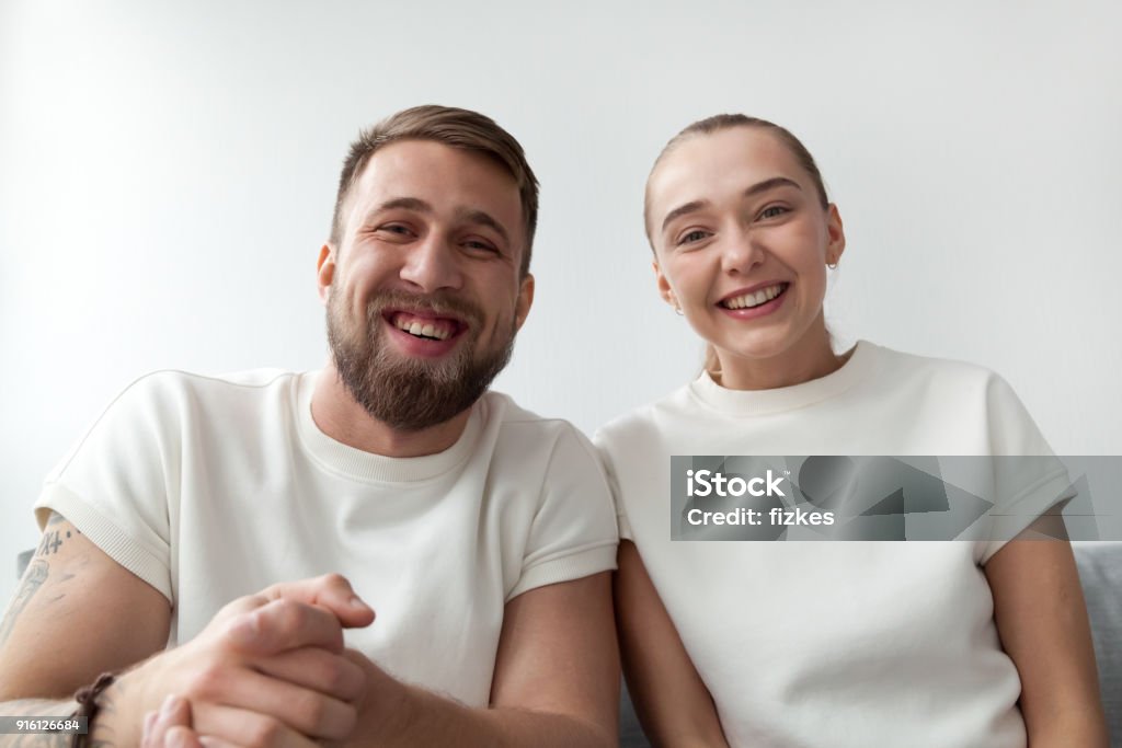 Smiling young couple looking at camera, making videocall, webcam Smiling young couple with happy faces looking at web camera, man and woman making videocall to distance friend by skype, funny vloggers recording videoblog or video message, webcam view portrait Webcam Stock Photo
