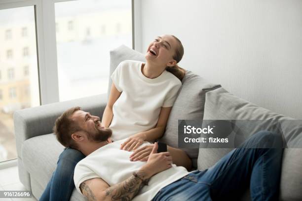 Cheerful Happy Couple Laughing With Joy Relaxing At Home Togethe Stock Photo - Download Image Now