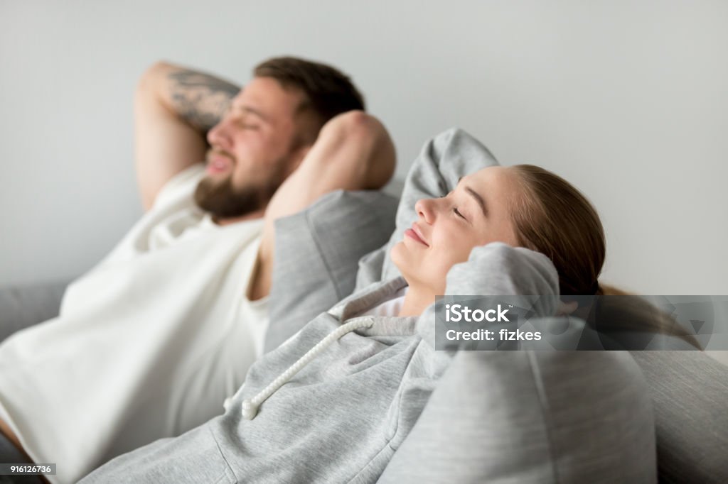Relaxed young couple relaxing on comfortable sofa together at ho Relaxed young couple resting on comfortable sofa together at home, happy woman smiling breathing fresh air leaning on soft cushion of new couch, man and woman enjoying nap relaxing or meditating Wind Stock Photo