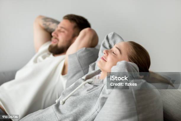 Relaxed Young Couple Relaxing On Comfortable Sofa Together At Ho Stock Photo - Download Image Now