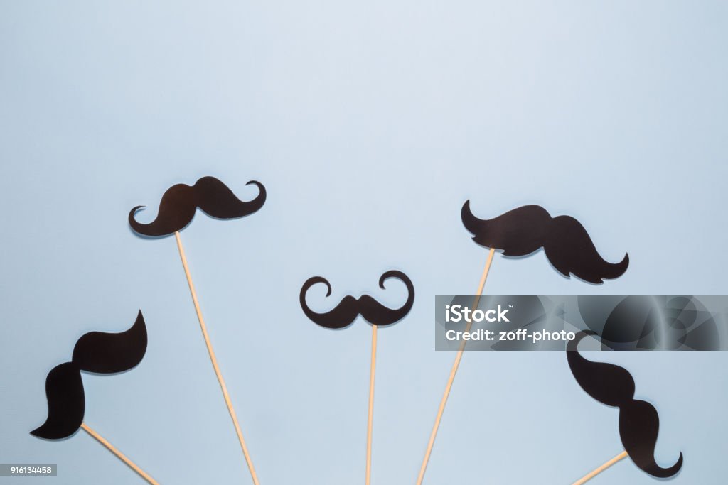 Flat lay of different kinds of paper mustaches against blue background Paper prop mustached in form of birds flying up in the sky abstract minimal concept Mustache Stock Photo