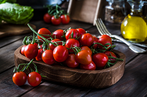 Fresh organic cherry tomatoes in a wooden tray shot on rustic wooden kitchen table. This vegetable is considered a healthy salad ingredient. Predominant colors are red and brown. Low key DSRL studio photo taken with Canon EOS 5D Mk II and Canon EF 100mm f/2.8L Macro IS USM