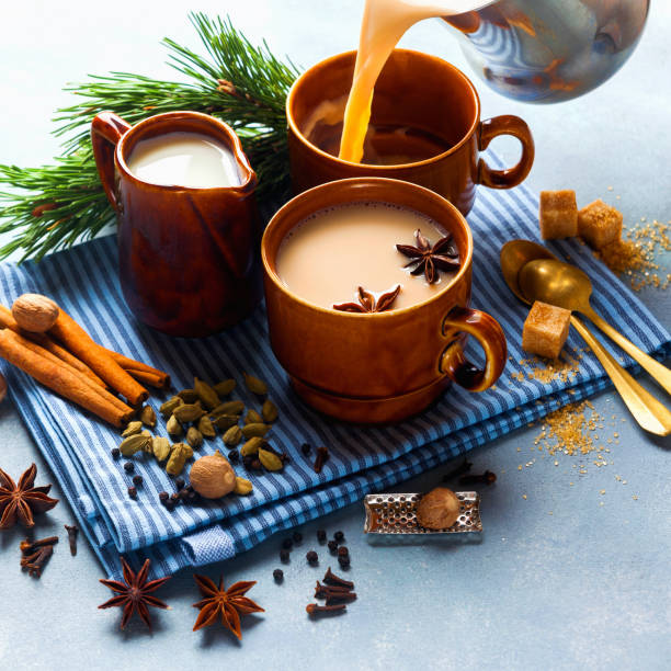 wylewanie masala herbaty chai latte tradycyjne gorące indyjskie teatime ceremonii słodkie mleko z przyprawami, zioła organiczne napar zdrowy napój w porcelanowej filiżance n niebieski tle tabeli. - cardamom indian culture food spice zdjęcia i obrazy z banku zdjęć